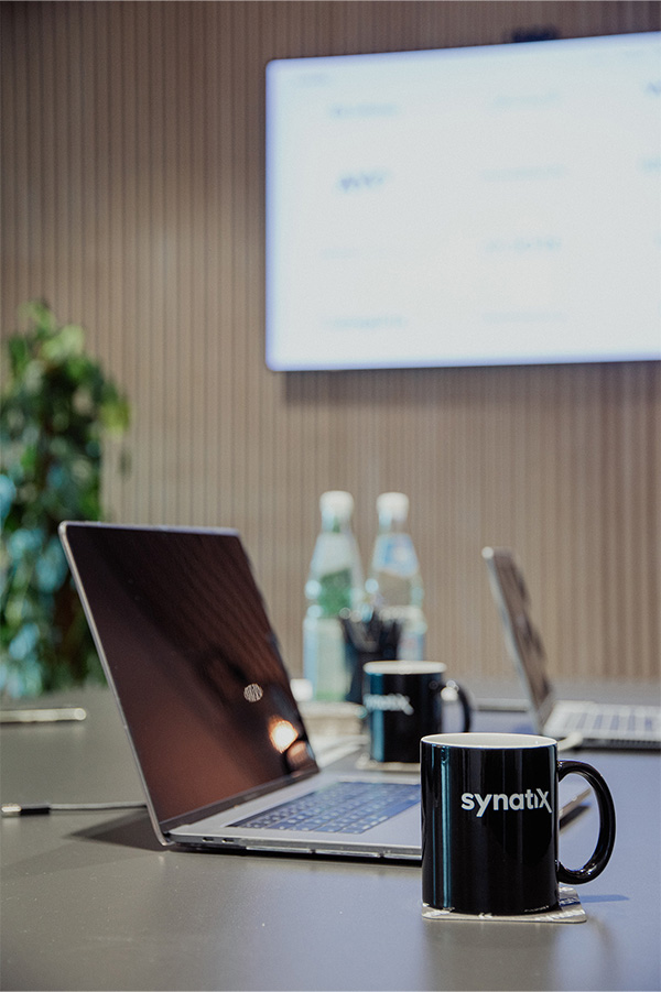 Laptop steht auf einem Tisch und eine Synatix Tasse ist im Vordergrund